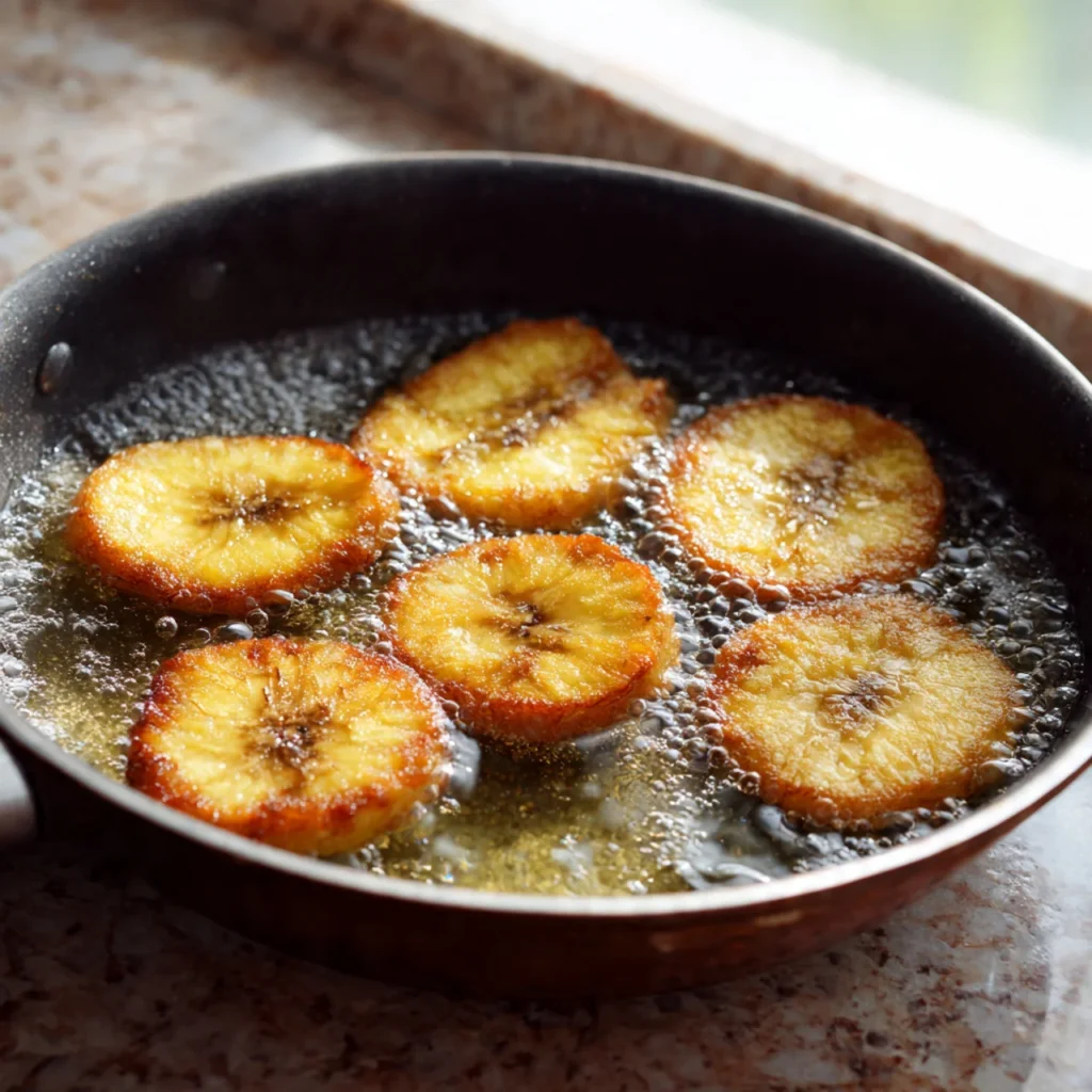 Green plantain slices frying for crispy tostones first fry